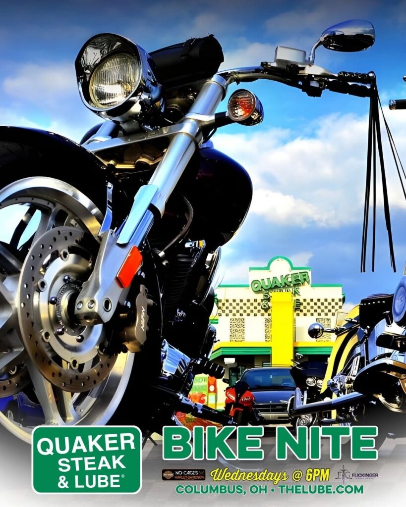 Close-up, low-angle view of a shiny black motorcycle with a Quaker Steak & Lube Bike Nite poster and venue in Columbus, Ohio in the background.